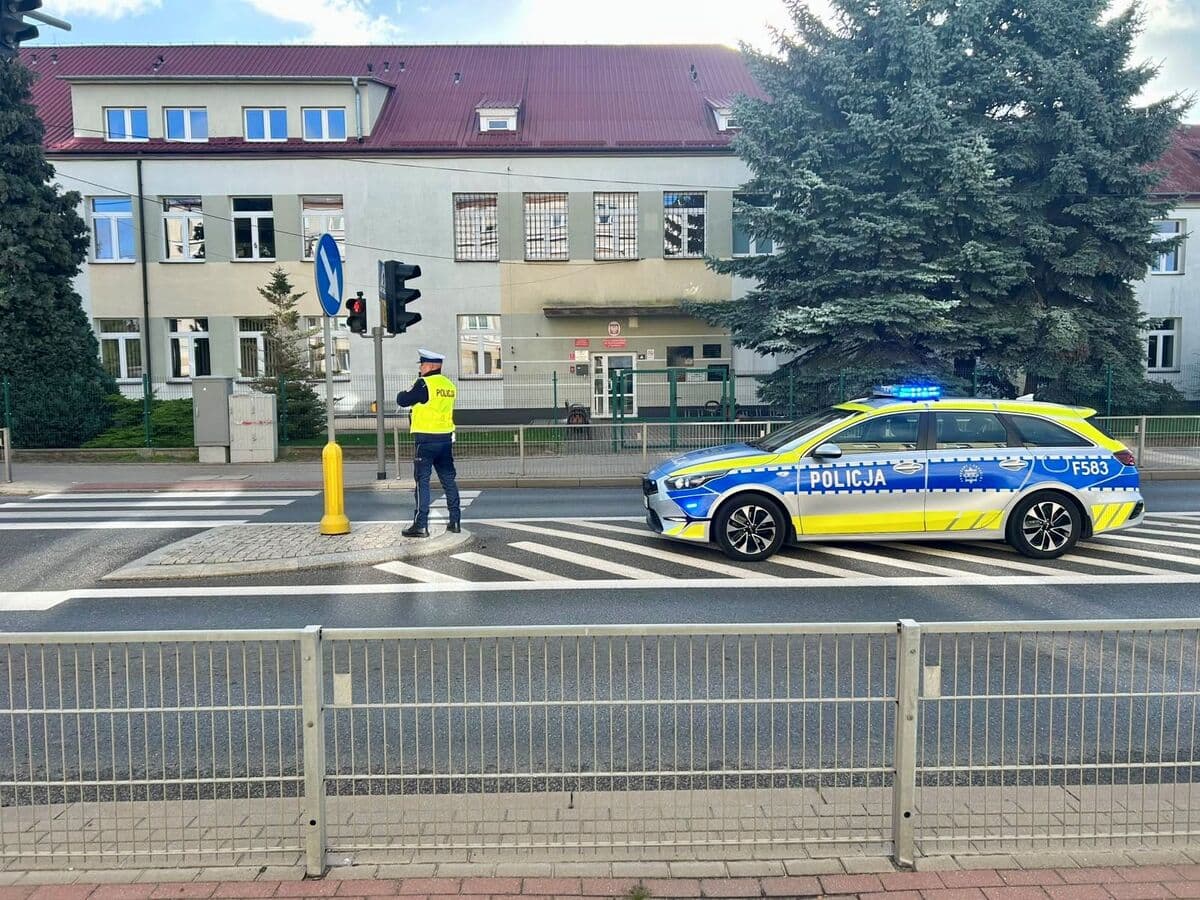 Radiowóz i policjant przy przejściu dla pieszych przed szkołą w powiecie poddębickim
